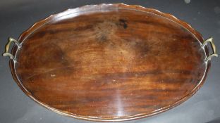 A George III mahogany oval drinks tray, the shaped rim with brass scroll work handles, 76 cm x 49.