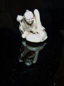 A Japanese Meiji period carved ivory netsuke as a mask maker, seated with a giant mask,