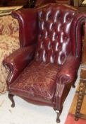 A pair of modern oxblood buttoned upholstered wing back scroll armchairs in the Georgian manner