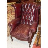 A pair of modern oxblood buttoned upholstered wing back scroll armchairs in the Georgian manner