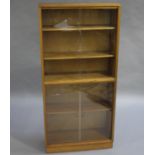 A sapele mahogany bookcase, 1960s, with two pairs of glass sliding doors, and five shelves,