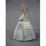 A Lladro figure of a young girl arms behind her back,