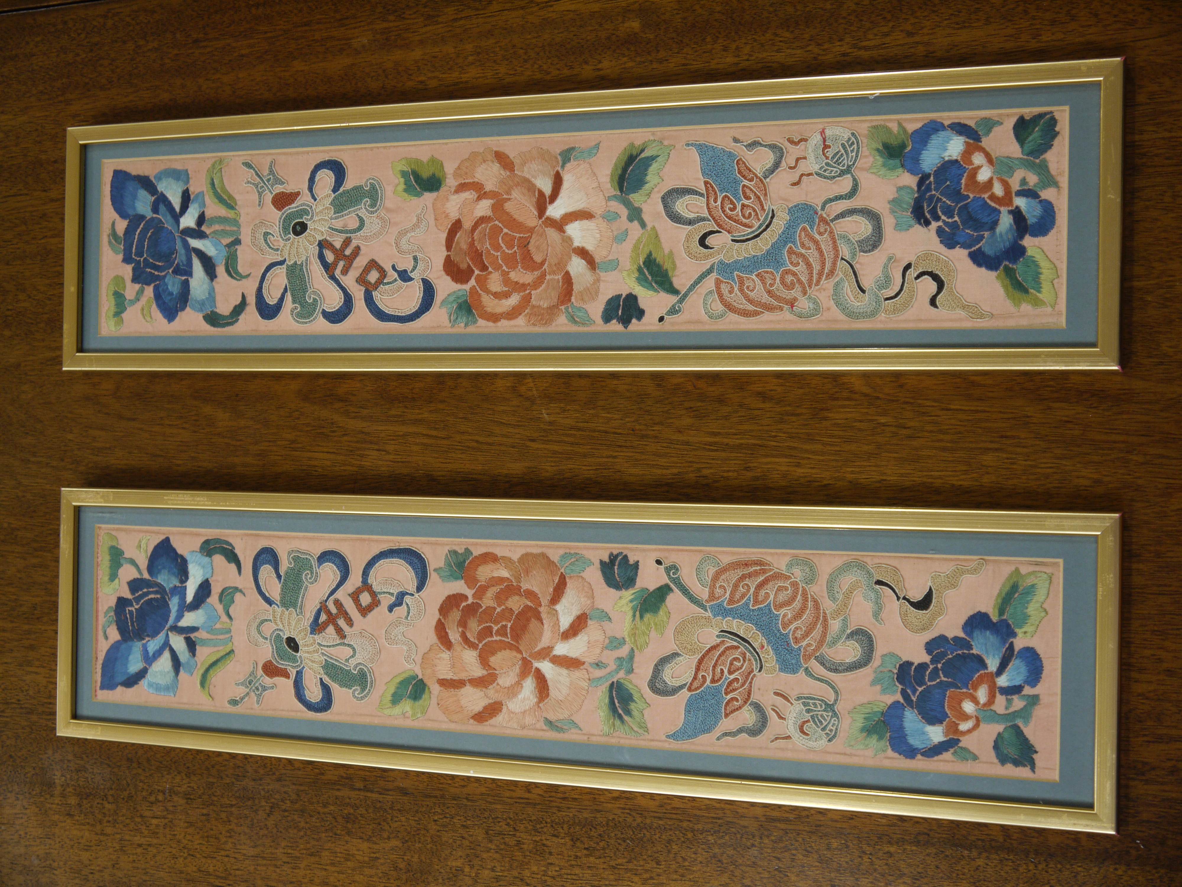 A pair of Chinese embroidered panels, worked with flower heads and leafage on a coral pink ground,