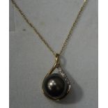 A cultured pearl and diamond set pendant the stained grey pearl within a hoop of yellow metal hung