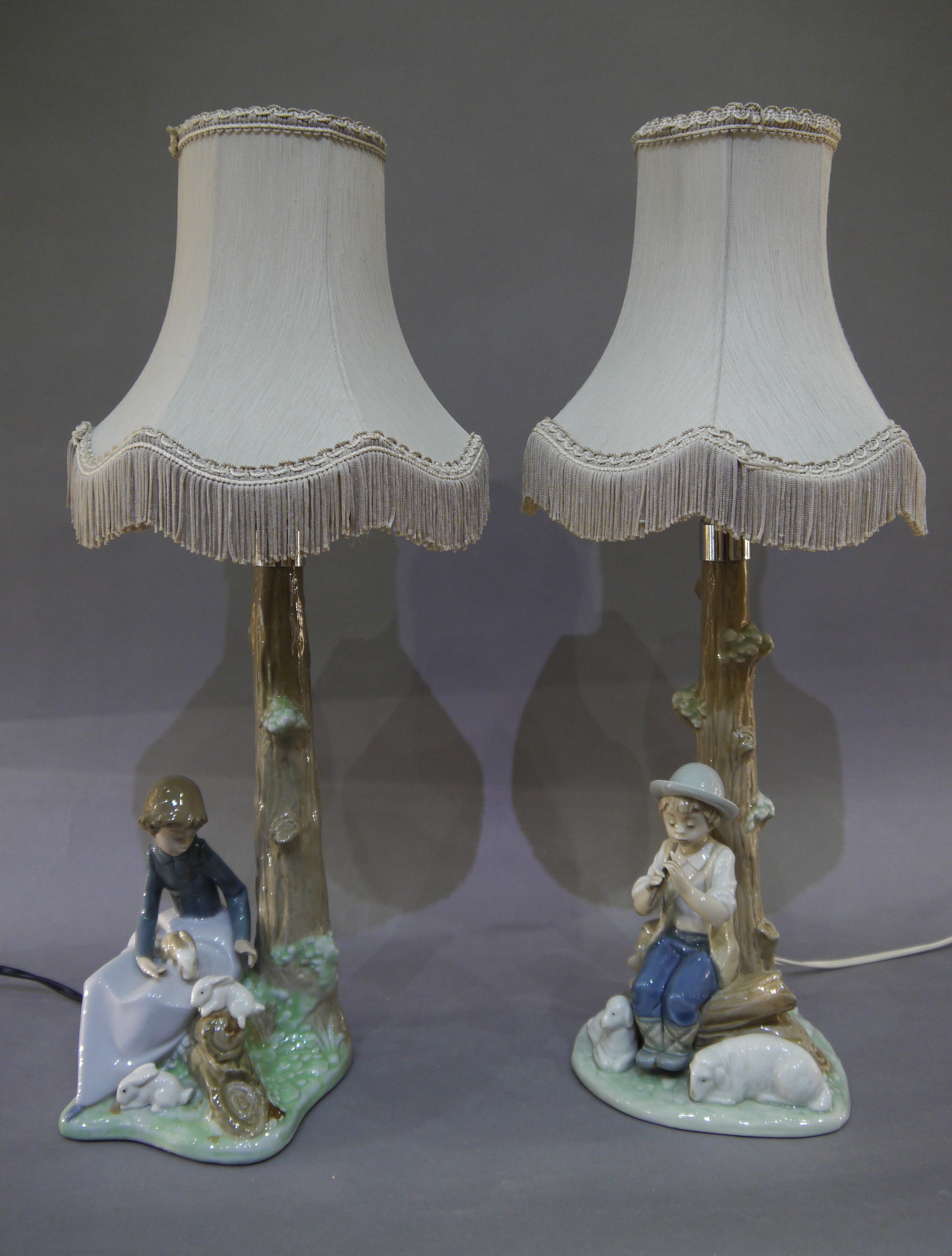 A pair of porcelain Nao table lamps, one modelled as a female seated with rabbits,