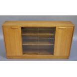 A 1960s teak bookcase having two glass sliding doors to the centre flanked by a cupboard to either