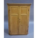 A 19th century pine corner hanging cupboard having a moulded and dentil cornice above two indented