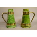 A pair of Arts and Crafts green glaze pottery and brass banded tankards of tapered cylindrical form,