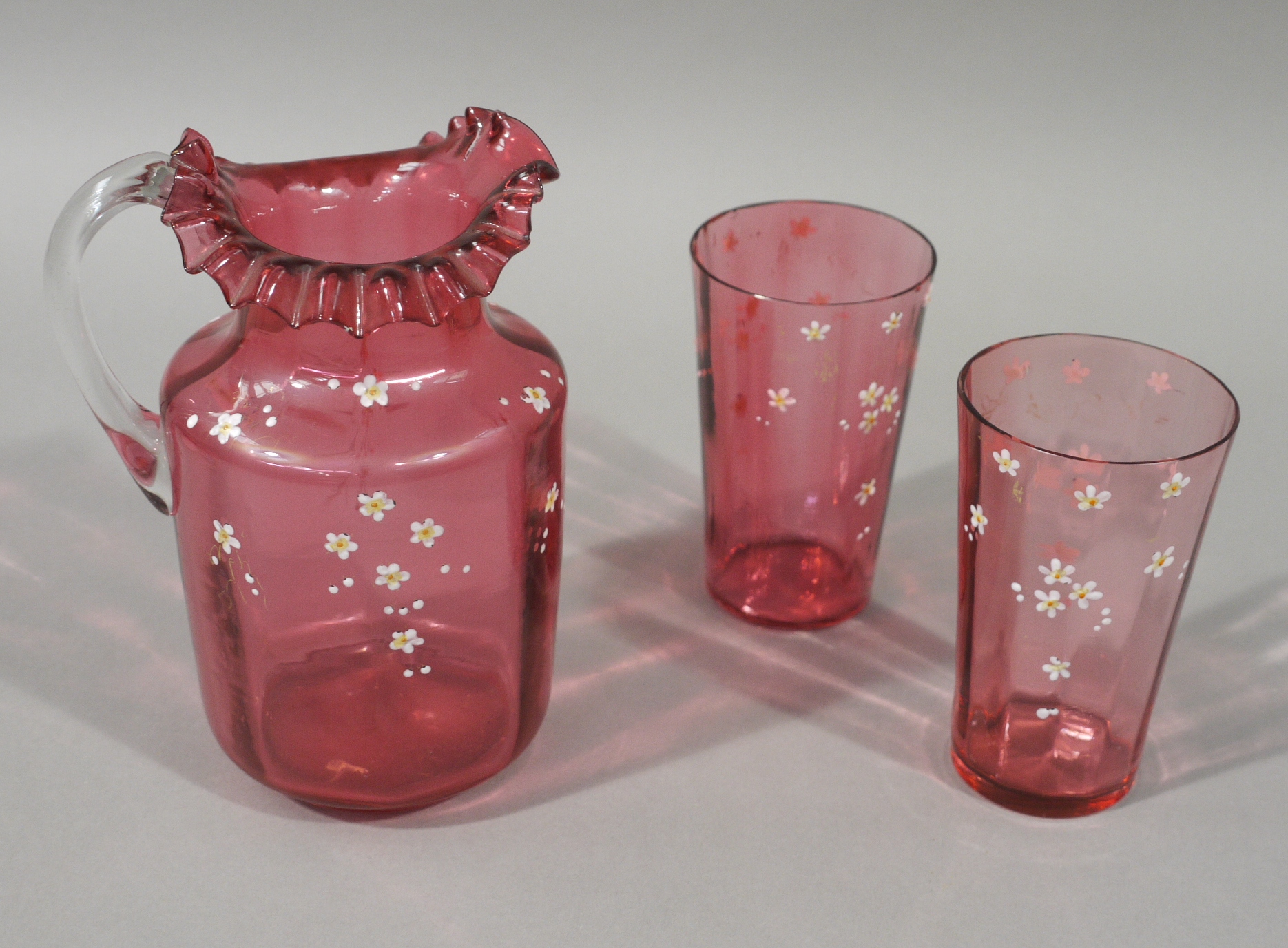 A Victorian cranberry glass jug and pair of matching tapered cylindrical beakers,