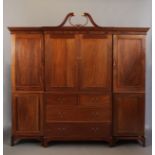 A reproduction mahogany breakfront wardrobe of George III style, having a broken swan neck pediment,