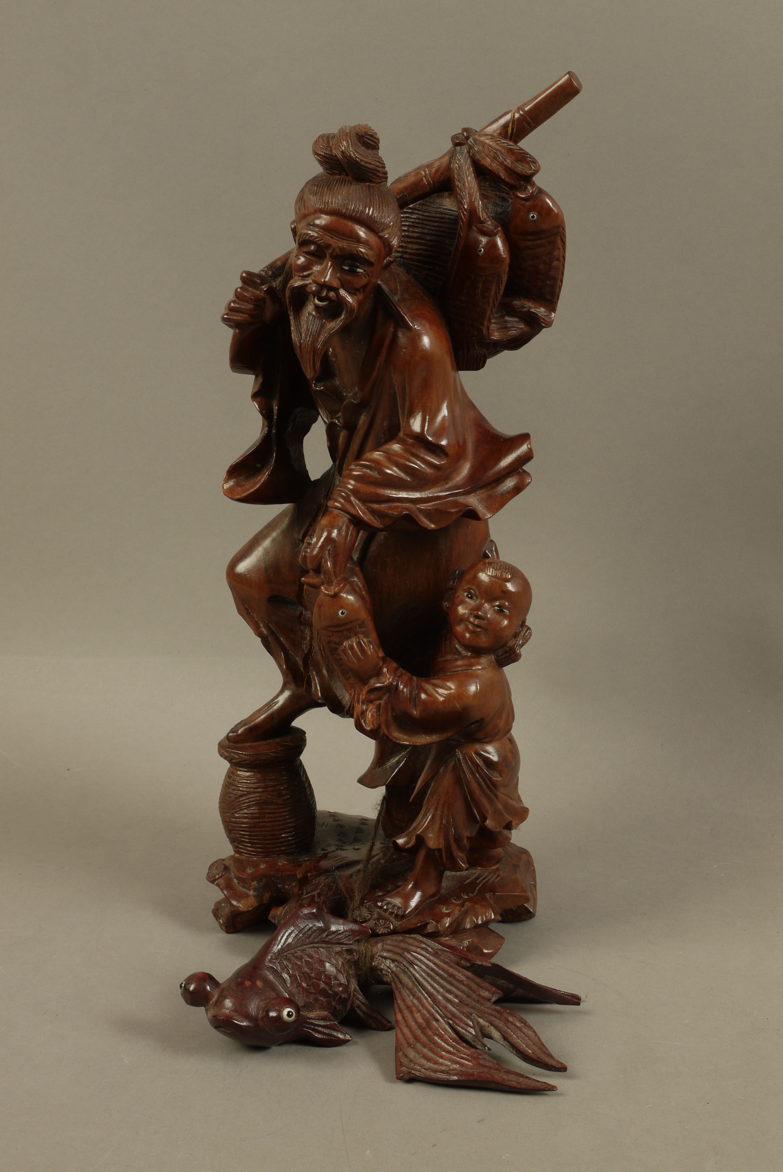 A Chinese hardwood figure of a bearded gentleman and infant holding fish over his shoulder and in