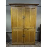 An Arts and Crafts oak cupboard having extended cornice above two indented panelled doors and two