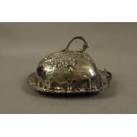 A silver plated butter dish and cover embossed with scrolls, flowerheads and leafage,