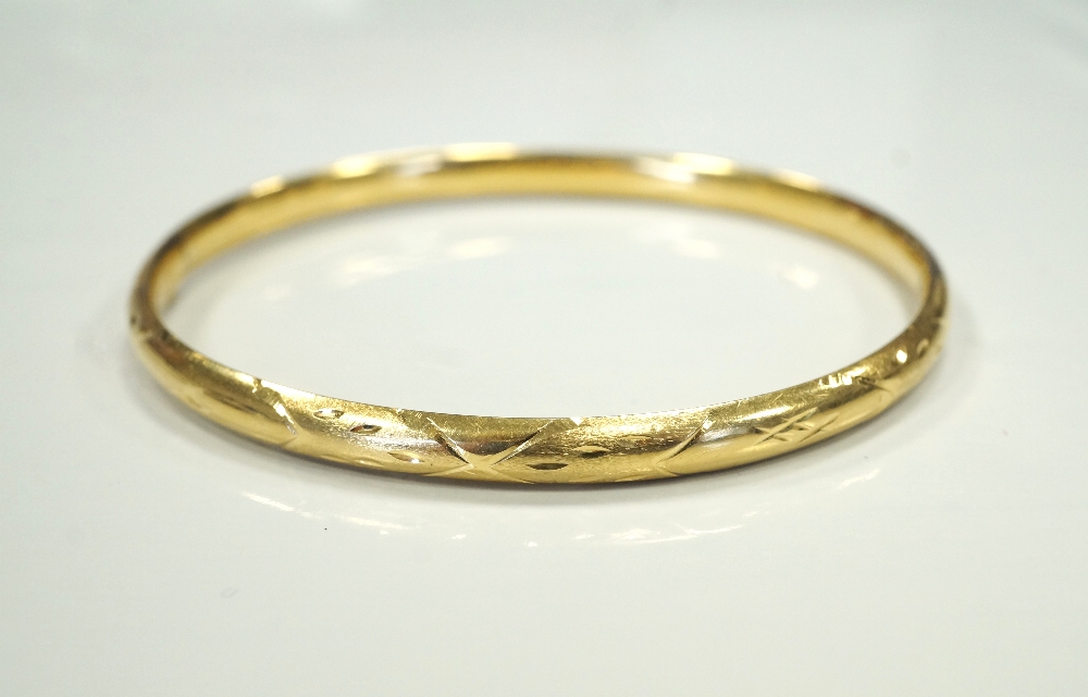 EIGHTEEN CARAT GOLD BANGLE with slide action safety clasp, with engraved decoration,