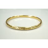 EIGHTEEN CARAT GOLD BANGLE with slide action safety clasp, with engraved decoration,