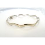 NINE CARAT WHITE GOLD BANGLE of wavy design with safety clasp, approximately 6.
