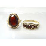 TWO GARNET RINGS one a solitaire ring in pierced and shaped setting and the other a cluster example,