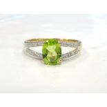 PERIDOT AND DIAMOND RING the central oval cut peridot flanked by diamond set split shoulders,