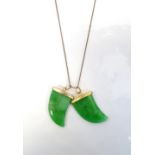 TWO JADE CLAW SHAPED PENDANTS with gilt mounts, on a nine carat gold chain,