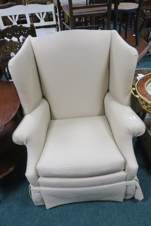 A BEIGE UPHOLSTERED WING CHAIR, with scroll arms and loose cushion.