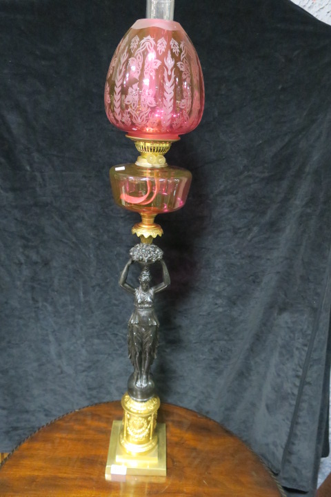 A VICTORIAN STYLE OIL LAMP the ruby glazed shade and reservoir supported by a black painted female