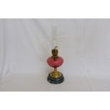 A 19th century oil lamp with ruby glass reservoir, brass stem and marble effect circular plinth