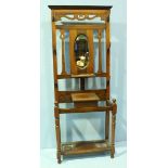 An early 20th Century walnut hall stand, with shaped cornice above an oval mirror, flanked by iron