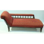 An Edwardian stained wood chaise lounge, with rouge fabric upholstery and raised on turned
