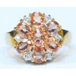 A 9ct gold Ceylon Padparadscha colour sapphire and diamond daisy cluster ring, set with 7 oval