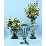 A group of 3 large modern flower vases of varying sizes, all on metal bases, one with two handles,