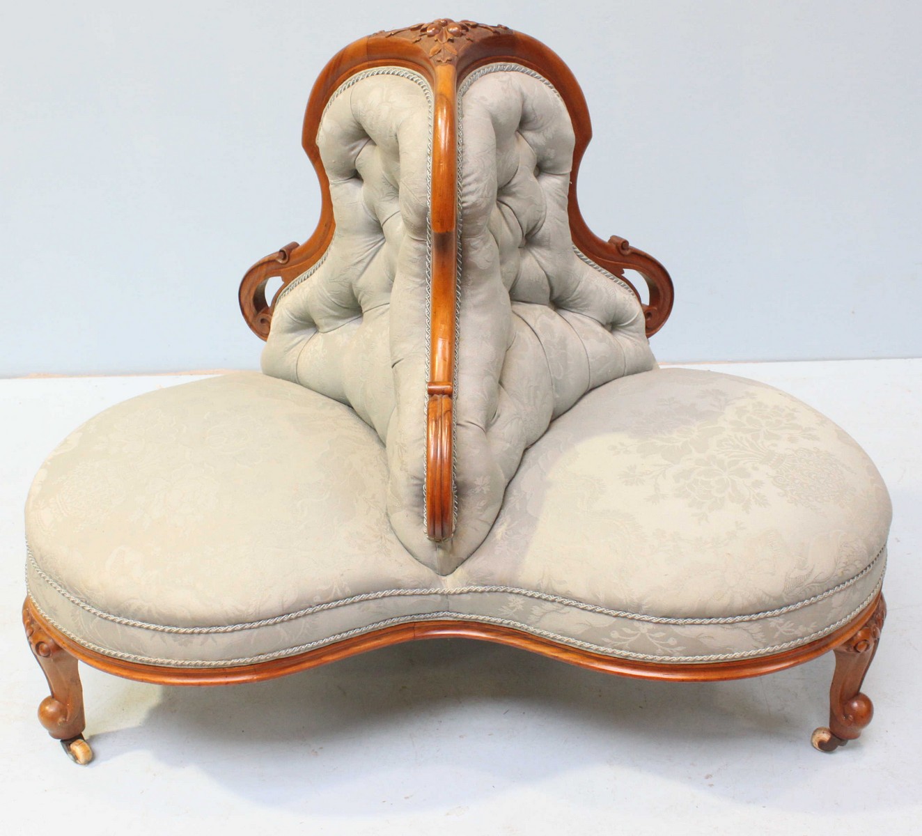 A Victorian walnut conversation sofa of trefoil form, with floral carved decoration, button back,