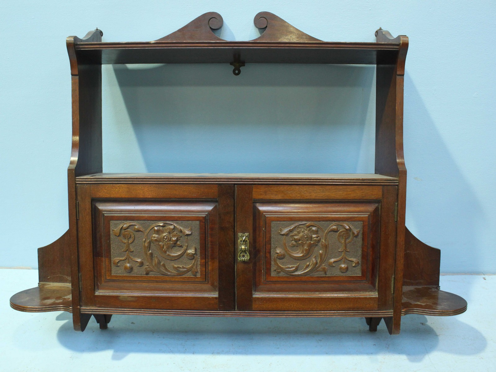 A mahogany wall cabinet, the scrolled top above an open shelf leading to two foliate carved panel