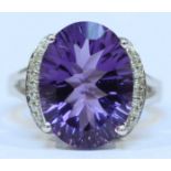 A 9ct white gold amethyst and diamond ring, claw set with a large central, oval amethyst, the