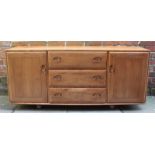 A 1960's elm Ercol sideboard, with three long central drawers, flanked by cupboard doors enclosing