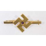 An 18ct gold bar brooch, the front decorated with a Buddhist symbol, centrally set with a round