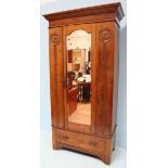 An Edwardian oak wardrobe, the shaped cornice above a single mirrored door opening to reveal hanging