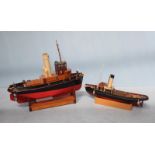 Two scratch built motorised model tug boats sitting upon stands, one lacking motor and named '