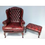 A burgundy leather wing backed Chesterfield armchair with brass studded detailing and raised on