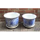 Two graduated blue and white ceramic jardinière pots and trays, decorated with floral designs. The