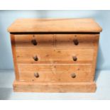 A stripped pine chest of two short, over two long graduated drawers, with turned pulls and raised on