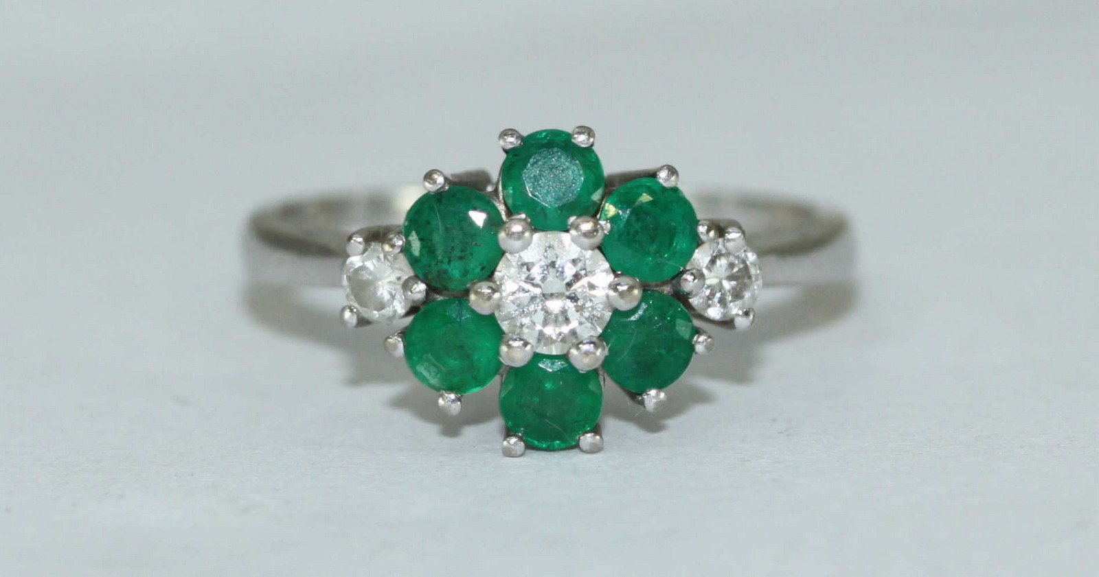 An 18ct white gold, diamond and emerald cluster ring, flower design, three diamonds estimated 0.