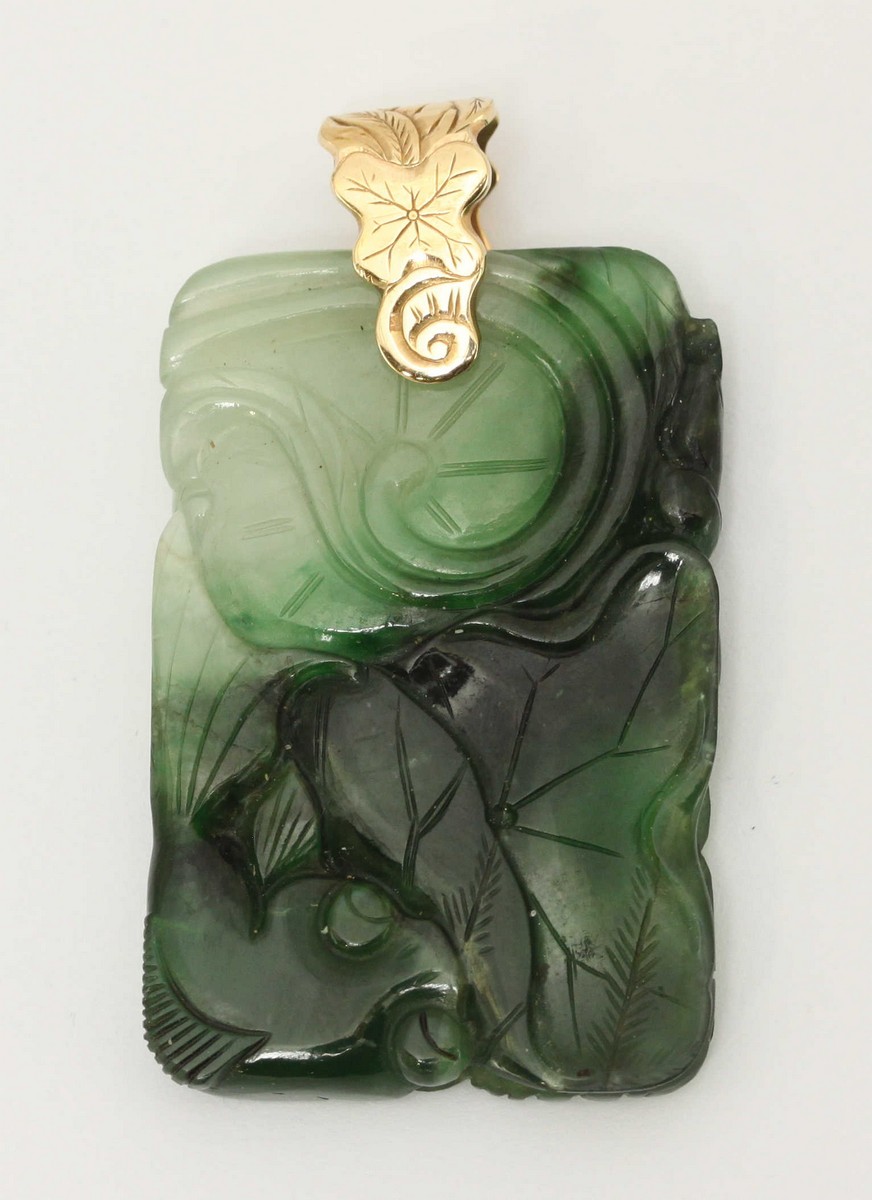 An carved jade pendant, ornately decorated with scrolls and flowers, mounted on a carved yellow