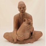 A 20th century terracotta figure of a seated North African man, holding a jug. 36cm high.