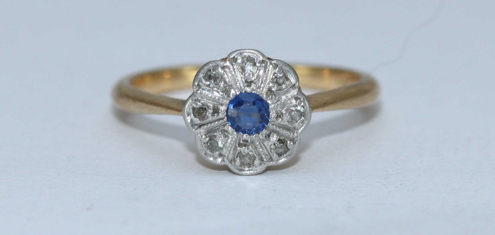 An 18ct gold, sapphire and diamond daisy cluster ring, rub-over setting, central sapphire surround