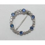 An 18 carat white gold open circle brooch set with six sapphires and eighteen diamonds. The