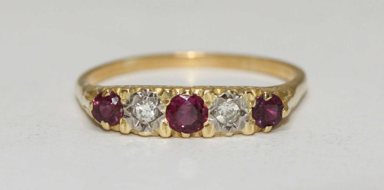 An 18 carat gold antique style ring with carved mount set with three rubies and two diamonds.