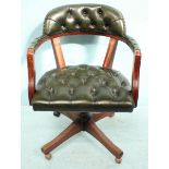 A swivel chair with green, deep button leather upholstery, brass studded detailing and raised on