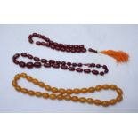 A reconstituted light amber oval bead necklace together with two dark simulated amber necklaces