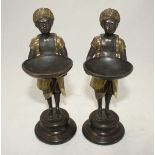 A pair of Blackamore bronze figures holding bowls, with gilt decoration and raised on turned