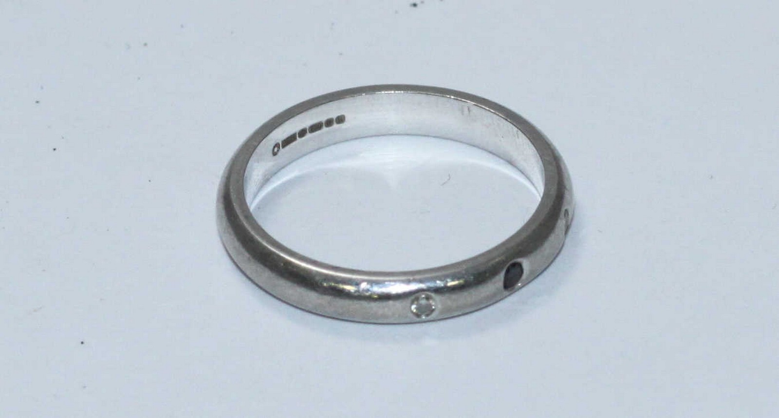 An 18ct white gold wedding ring, the band set with a small black diamond flanked by two small - Image 2 of 2